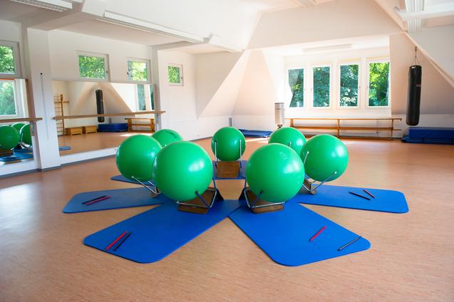 Fitnessraum mit grünen Gymnastikbällen auf blauen Matten, umgeben von Spiegeln und Fenstern.